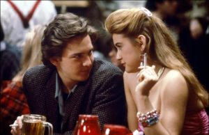 Sony To Celebrate The 40th Anniversary Of ‘St. Elmo’s Fire’ With 4K UHD Blu-Ray This June A young man and woman sit closely at a table in a crowded restaurant or bar, looking at each other intently, with drinks and red table decorations in front of them.