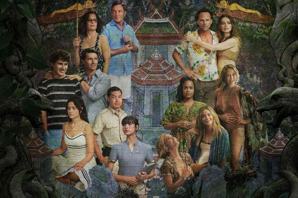 A group of thirteen people posed in front of an ornate temple-like backdrop. The group includes a mix of men and women, casually dressed, with lush greenery surrounding the scene.