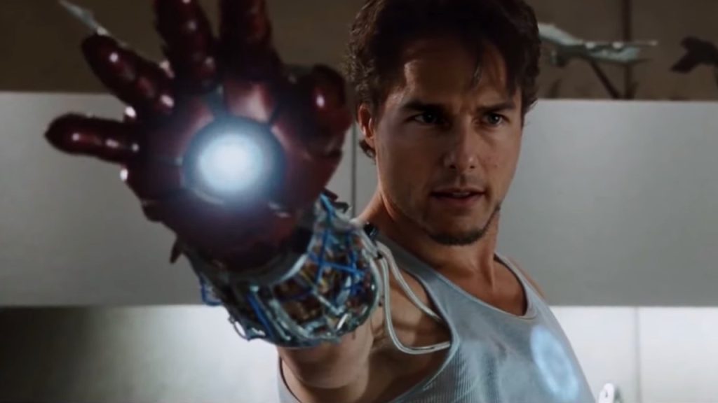 A man in a tank top holds out a mechanical arm with a glowing light in the palm, looking forward with a determined expression.