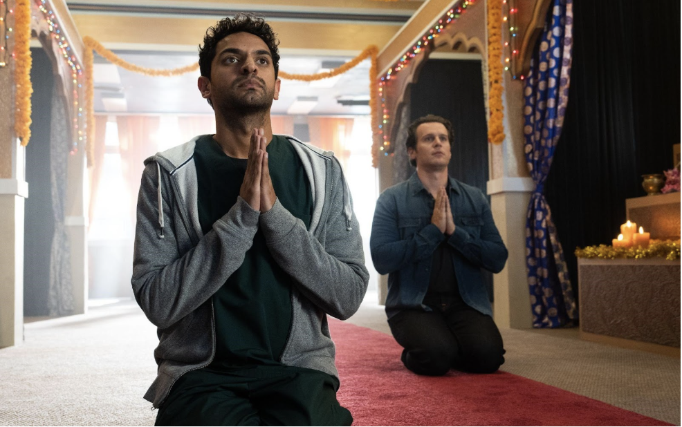 Two people kneeling in prayer on a carpeted floor in a decorated room, with decorative lights and orange garlands hanging above.
