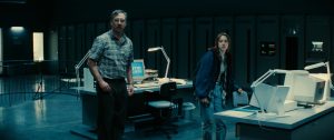 XYZ Films & Flawless Release New Clip From Sci-Fi Adventure ‘Watch The Skies’ Ahead Of Theatrical Debut (EXCLUSIVE) A man and a woman stand in a dimly lit office with desks, computers, and large servers in the background.