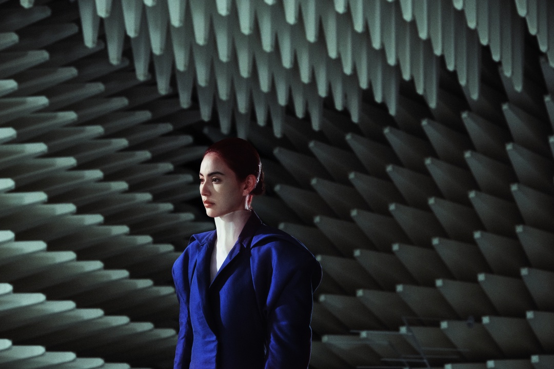 A person in a structured blue outfit stands in front of a patterned wall with large, gray, geometric foam panels.