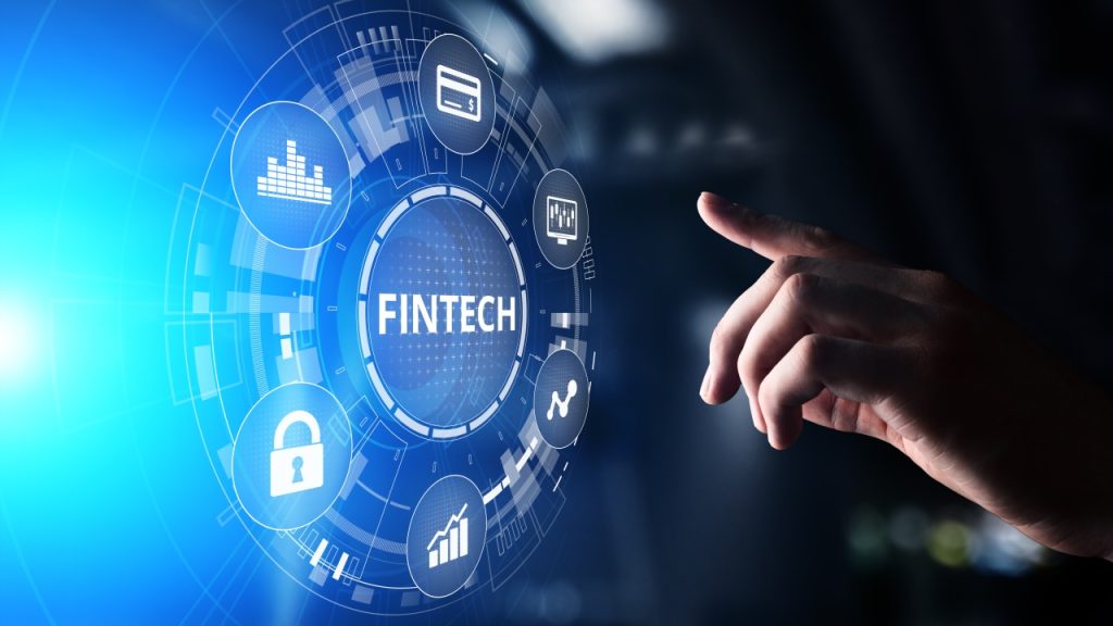 A hand points at a digital interface displaying the word "Fintech" surrounded by icons representing finance and technology concepts.