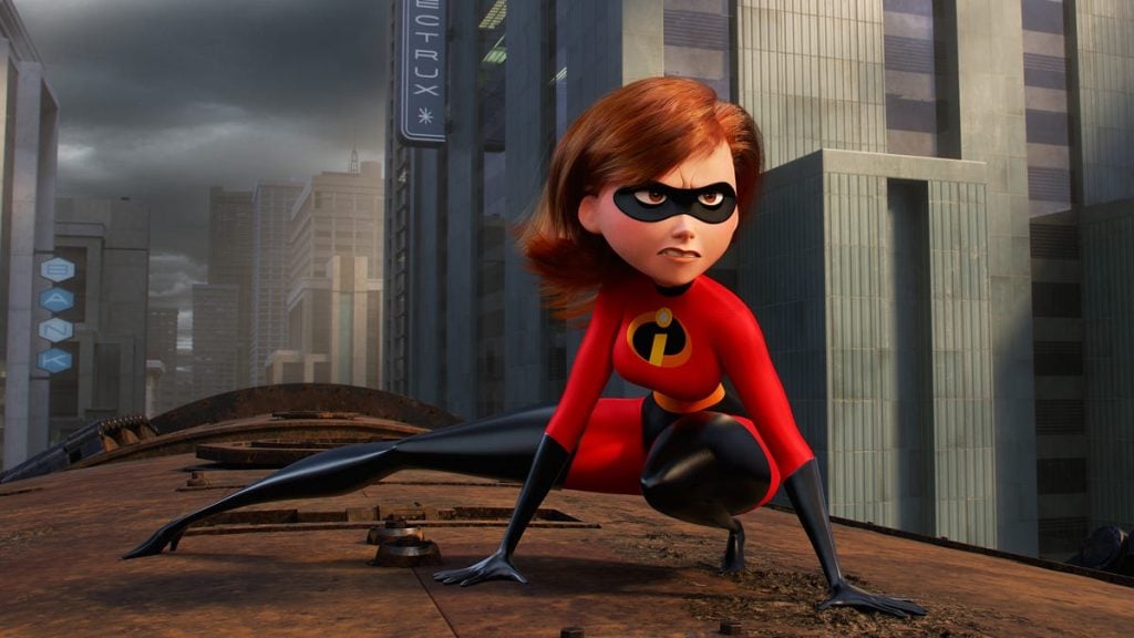 Animated superhero in a red and black costume crouches on a rooftop in a city, wearing a mask and looking alert, with tall buildings in the background.