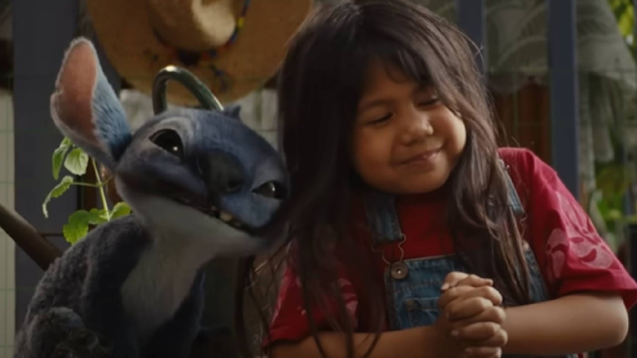 A smiling young girl in overalls stands next to a blue alien creature with large ears, both appearing happy and friendly.
