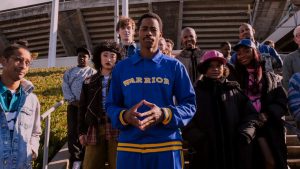 Lionsgate To Release The Pulpy ‘Freaky Tales’ On 4K UHD Blu-Ray In Throwback VHS Packaging This June A group of people stands outdoors on steps, with a man in a blue "Warrior" jacket posed at the center in front of a stadium.