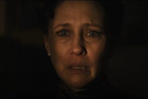 A woman with a worried expression looks ahead in dim lighting, her face partially illuminated, highlighting her anxious eyes and slightly parted lips.