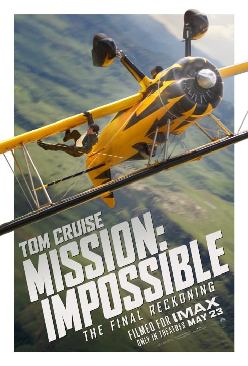 A person hangs onto the side of a yellow biplane in flight above green fields; the text promotes "Mission: Impossible – The Final Reckoning," starring Tom Cruise, opening May 23 in IMAX.