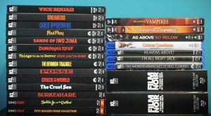 A collection of DVD and Blu-ray movie cases stacked in two columns against a blue background, showing various film titles on their spines.
