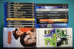 No Streaming Required: Physical Media Spotlight For The Week Of May 13th – Exploring The Warner Archive A collection of Blu-ray and DVD cases, organized in three upright stacks and two lying flat, featuring various movie and TV titles, including "Ben 10," "Dune," and "Dirty Harry.