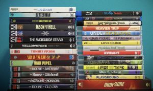 Two stacks of assorted DVD and Blu-ray movie cases are arranged vertically against a teal background, showing various film titles on their spines.