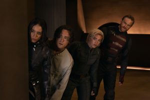 Four people in tactical gear cautiously peek around a corner inside a dimly lit building.