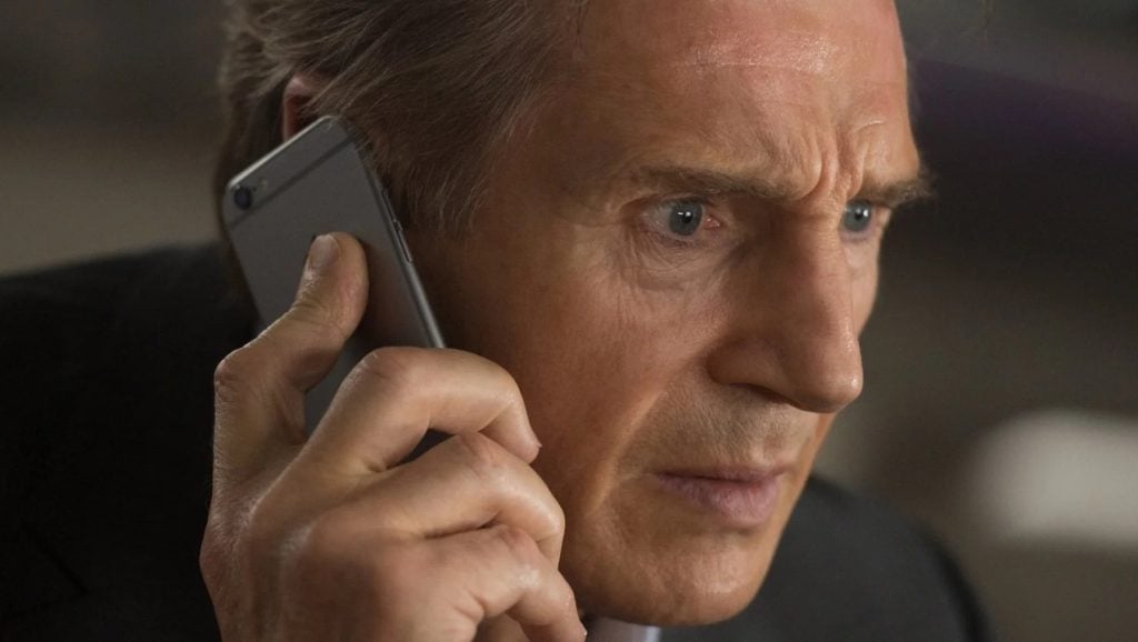 A man with a serious expression holds a smartphone to his ear, appearing to listen intently during a phone call.