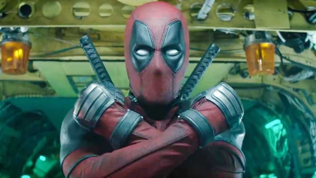 A person in a red and black superhero suit with crossed arms stands in front of a mechanical background, with two swords on their back.