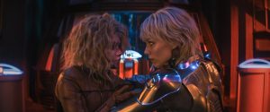 Universal To Release The Sci-Fi Sequel ‘M3GAN 2.0’ On 4K UHD Blu-Ray In A New Unrated Form This September Two women in futuristic suits face each other closely in a dimly lit, high-tech environment with vibrant red and blue lighting.