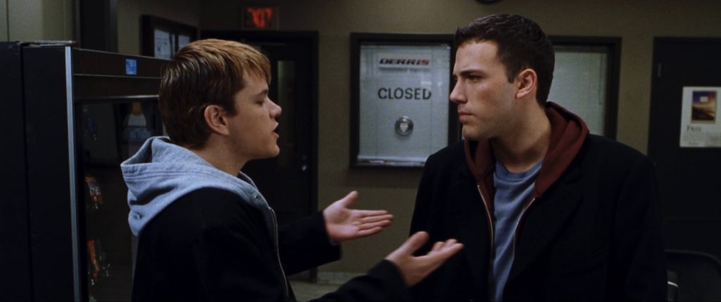 Two men stand indoors; one gestures with open hands while the other listens with a serious expression. A "CLOSED" sign is visible on the door behind them.