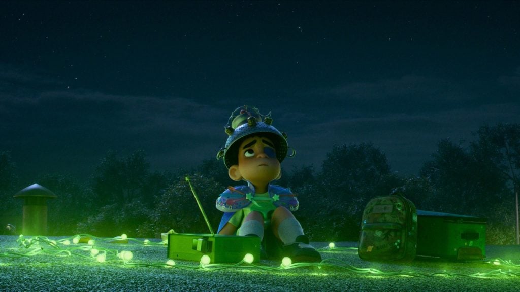 An animated child wearing a homemade helmet sits on a rooftop at night, surrounded by green glowing string lights, with a backpack and some equipment nearby.