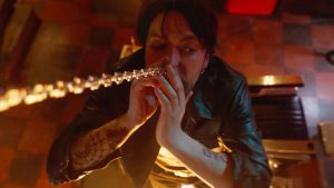 A person in a leather jacket is using a rolled-up bill to snort a substance laid out in a line on a reflective surface.