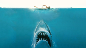 Celebrating 50 Years of ‘Jaws’: A Cinematic Milestone That Redefined Fear A swimmer at the surface of the water is unaware of a large shark with an open mouth approaching from below.