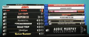 A collection of DVD and Blu-ray movie cases stacked in two columns, including titles like "JAWS," "Law and Order," and "AUDIE MURPHY COLLECTION V.