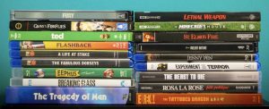 Two vertical stacks of assorted Blu-ray and 4K Ultra HD movie cases, with various film titles visible on their spines against a blue background.