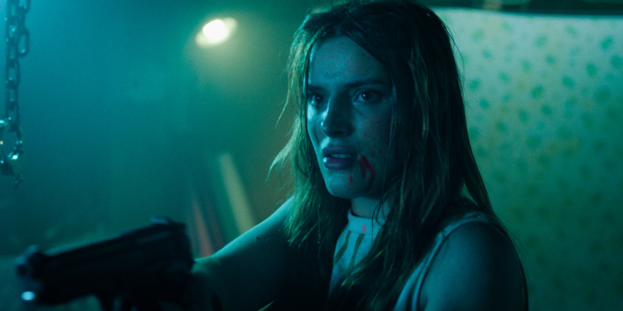 A young woman with blood on her face points a gun, standing in a dimly lit room with a tense expression.