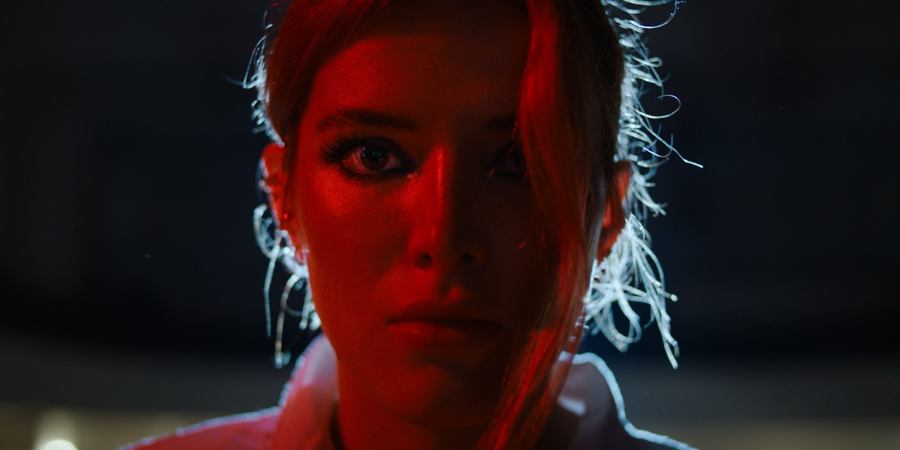 Close-up of a person with intense expression, lit by a strong red light from the side, with some strands of hair illuminated by backlight.