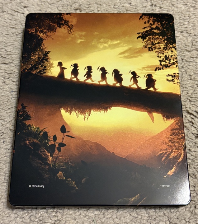 A group of seven dwarfs walks in a line across a log bridge at sunset, silhouetted against a golden sky and forested landscape.