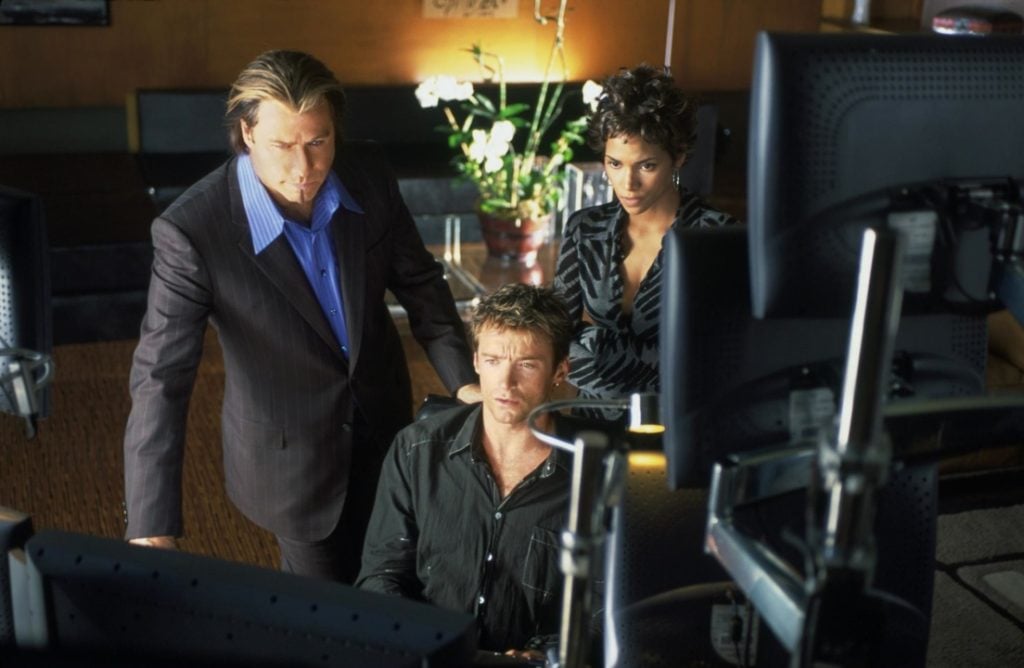 Three people in business attire stand closely together, focused on multiple computer monitors in a modern office setting.