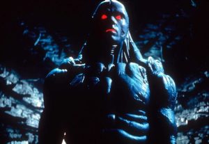Imprint & Via Vision Announce 4K UHD Blu-Ray Releases Including Titles From David Lynch, Keanu Reeves & More A humanoid figure with glowing red eyes and a muscular, armored body stands in a dim, blue-lit environment.