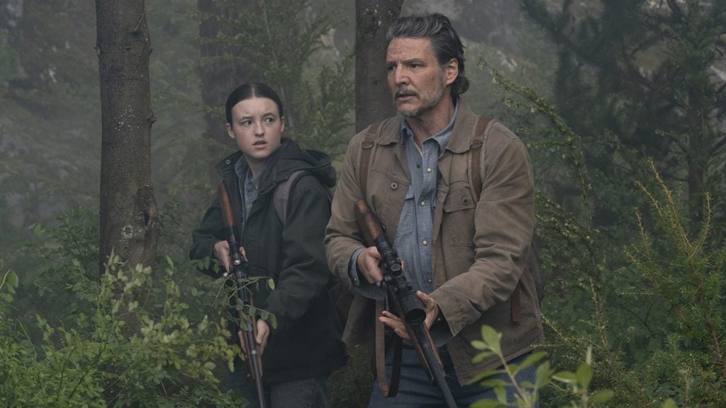 Two people holding rifles move cautiously through a dense forest, appearing alert and focused.