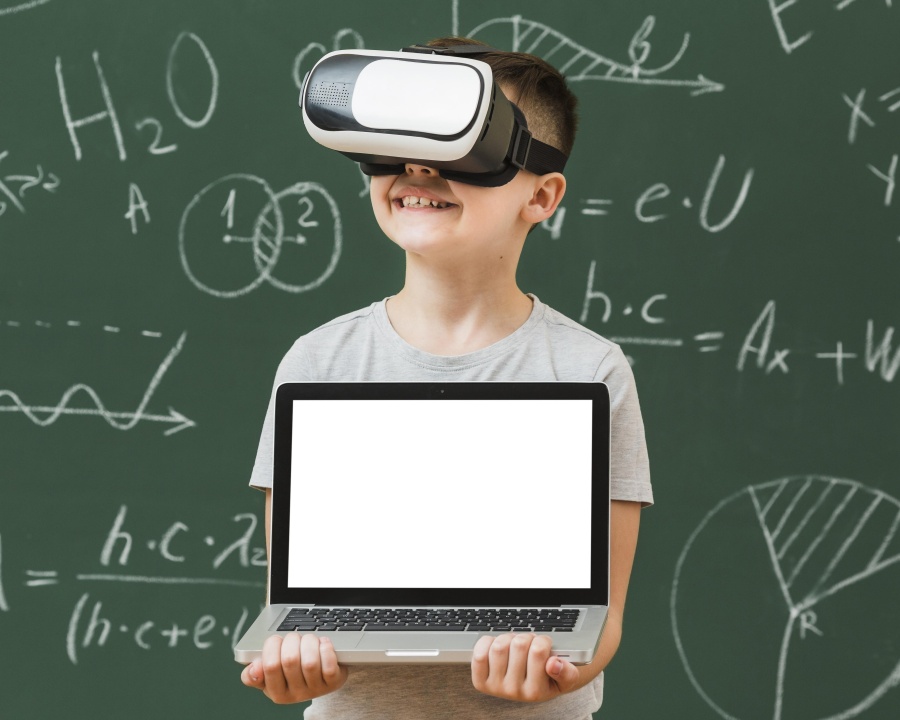 A child wearing a VR headset holds a laptop with a blank screen, standing in front of a chalkboard covered in math and science formulas.