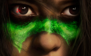 Close-up of a person's face with intense eyes, a streak of glowing green paint across the nose and cheeks, and a reflection of red light in the left eye.