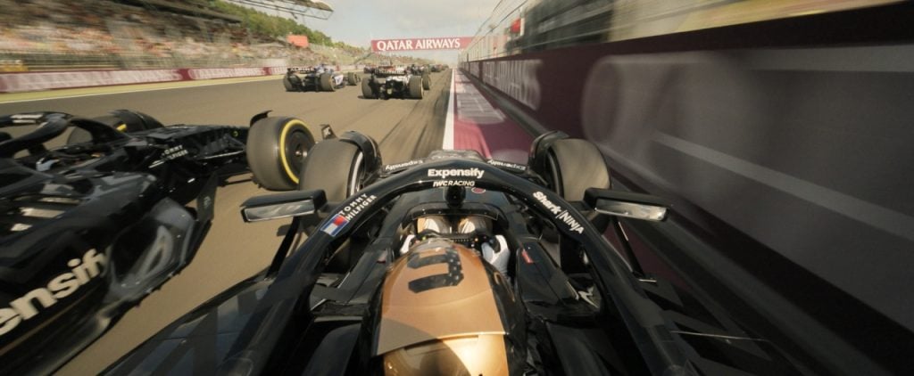 Onboard view from a Formula 1 car during a race, surrounded by other cars on a track, with a blurred background indicating high speed.
