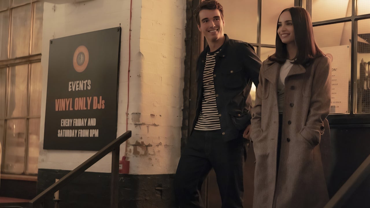 A man and a woman stand outside a building near a sign advertising vinyl-only DJ events on Fridays and Saturdays from 11 PM.