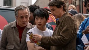 Sony To Release A Six Film ‘Karate Kid’ 4K UHD Collection This August In Tandem With ‘Karate Kid: Legends’ Three people stand outdoors closely examining a ticket or flyer; the middle person looks surprised while the others appear focused and serious.