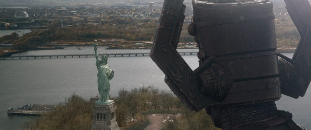 A giant robot towers over the Statue of Liberty, with a cityscape and river in the background.