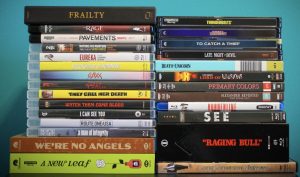 Stacks of DVD and Blu-ray movie cases, with film titles visible, arranged in three columns against a blue background.