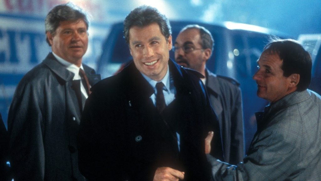 A man in a suit smiles while standing outdoors with three other men, all dressed in jackets, at night.