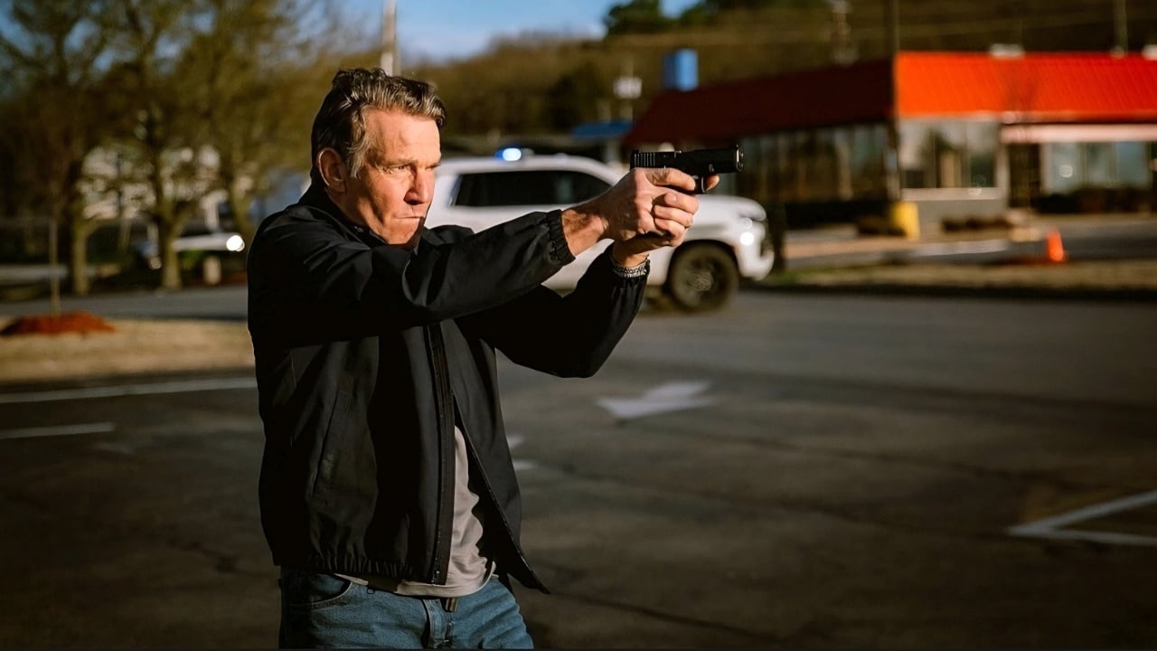 A man in a black jacket aims a handgun with both hands in a parking lot during daylight.