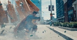 Warner Bros. To Release James Gunn’s ‘Superman’ On 4K UHD Blu-Ray This September A person in a superhero costume crouches on a city sidewalk as glass and debris explode around them in broad daylight.