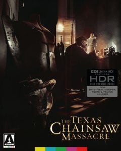 A man sits at a cluttered desk in a dimly lit room with mannequins, chains, and tools; "The Texas Chainsaw Massacre" is displayed at the bottom with 4K Ultra HD and HDR labels.