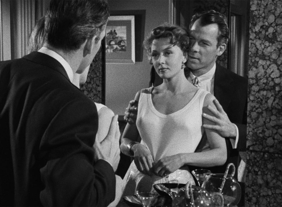A man and woman are reflected in a mirror as another man faces them; the setting appears to be an upscale room with drinks and marble surfaces.