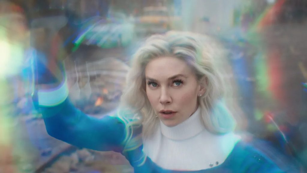 A woman with long blonde hair and a blue and white outfit stands with her hand raised, surrounded by a glowing, multicolored energy field.