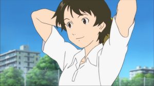 GKIDS & Shout! Studios To Release Mamoru Hosoda’s ‘The Girl Who Leapt Through Time’ On 4K UHD Blu-Ray Anime character with short brown hair and a white shirt ties her hair back outdoors, with trees, buildings, and blue sky in the background.