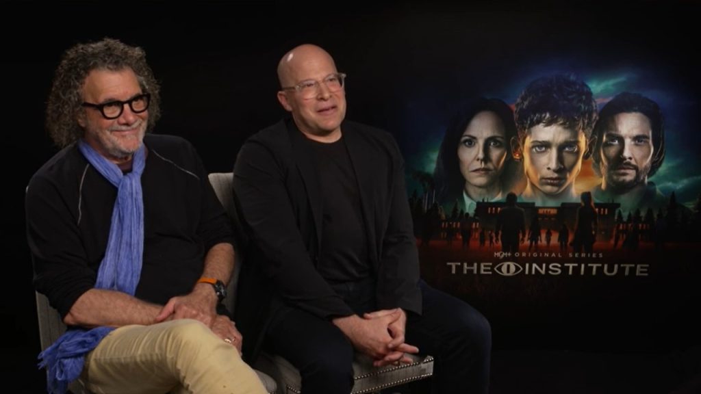 Two men sit for an interview beside a promotional poster for the HBO original series "The Institute," featuring three serious faces and a dark, atmospheric background.