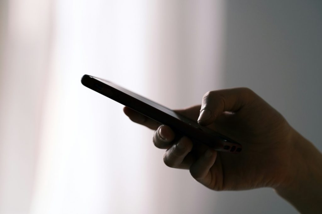 A hand holding and using a smartphone against a softly lit background.