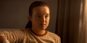 Bella Ramsey Being Eyed For Marvel’s X-Men Film? A young person with brown hair tied back sits indoors, wearing a beige and brown striped shirt, looking forward with a neutral expression.