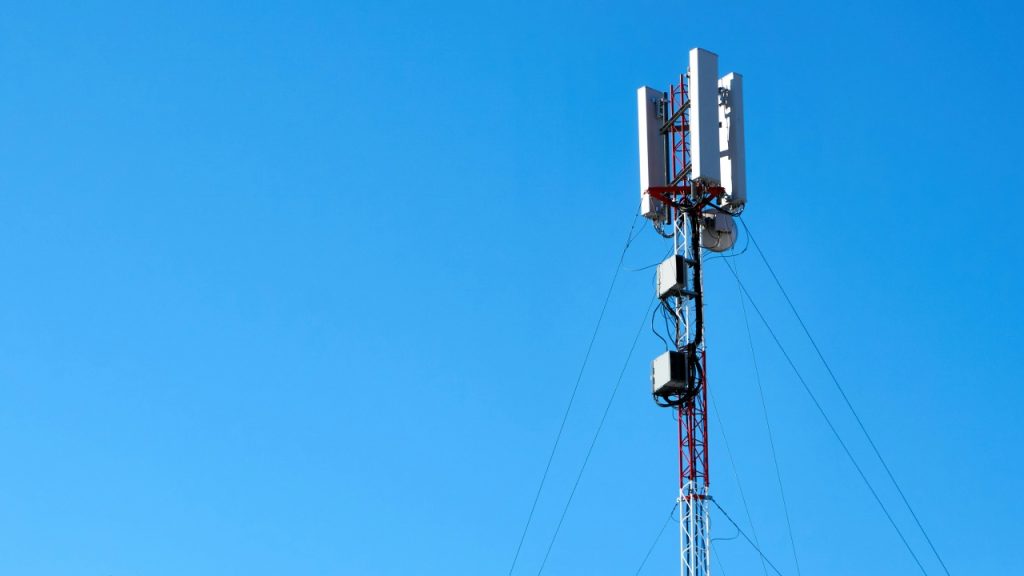 A cell tower with antennas and cables against a clear blue sky.