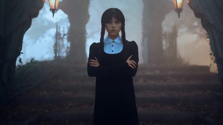 A young woman with long dark braids and a white collar dress stands with arms crossed on stone steps, surrounded by mist and gothic lanterns.